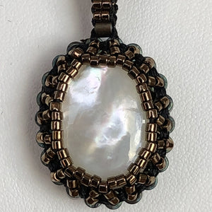 Mother of pearl cabochon framed by fine metallic bronze micro-beading