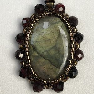 Labradorite cabochon cameo pendant framed by fine beading of metallic bronze micro-beads and garnet gemstone.