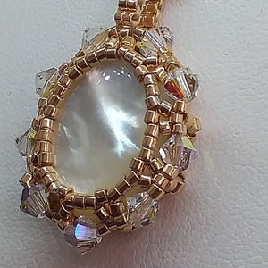 Mother of pearl cabochon pendant framed by fine beading of metallic champagne micro-beads and Swarovski crystal