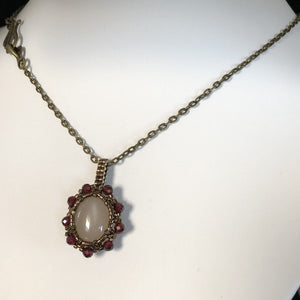 Opaque pink moonstone cabochon pendant framed by fine beading of metallic bronze micro-beads and facetted garnet