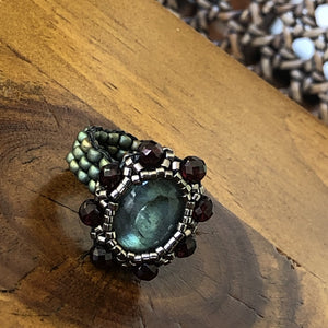 Beaded ring with labradorite centerpiece surrounded by facetted garnet and fine micro-beading. Mat teal beaded band.