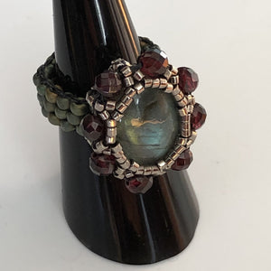 Beaded ring with labradorite centerpiece surrounded by facetted garnet and fine micro-beading. Mat teal beaded band.