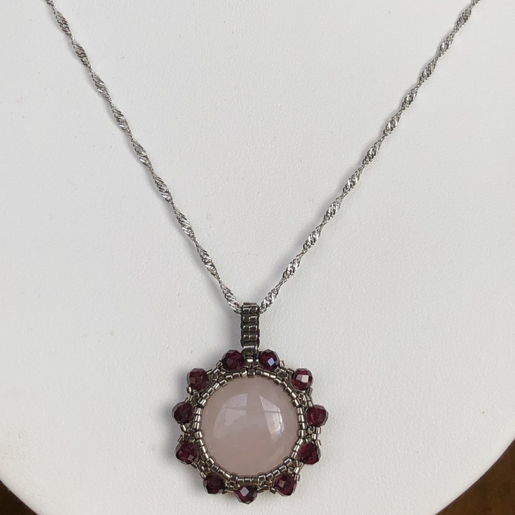 Rose quartz cabochon pendant framed by metallic steel-tone micro-beading with facetted garnet on a steel twisted French chain