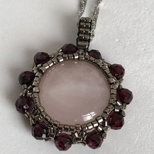 Rose quartz cabochon pendant framed by metallic steel-tone micro-beading with facetted garnet on a steel twisted French chain