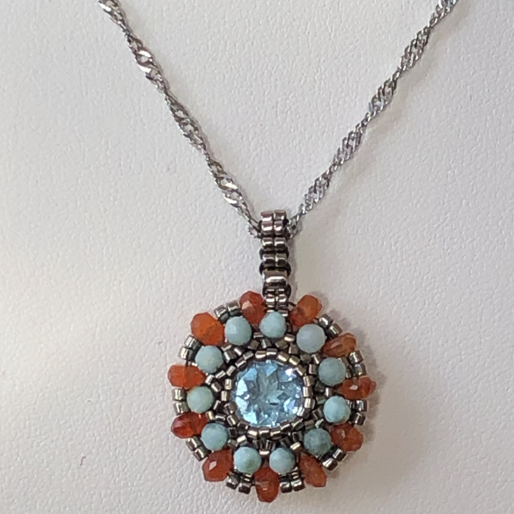 Beaded charm pendant with blue topaz center piece and mandala of larimar and carnelian with metallic steel micro-beading.
