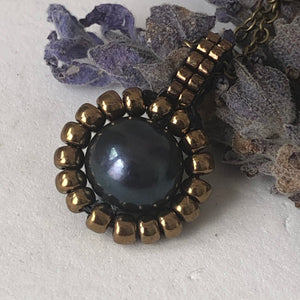 Pearl pendant necklace. Beaded jewellery. Large round freshwater black pearl surrounded by metallic bronze-tone glass beads.