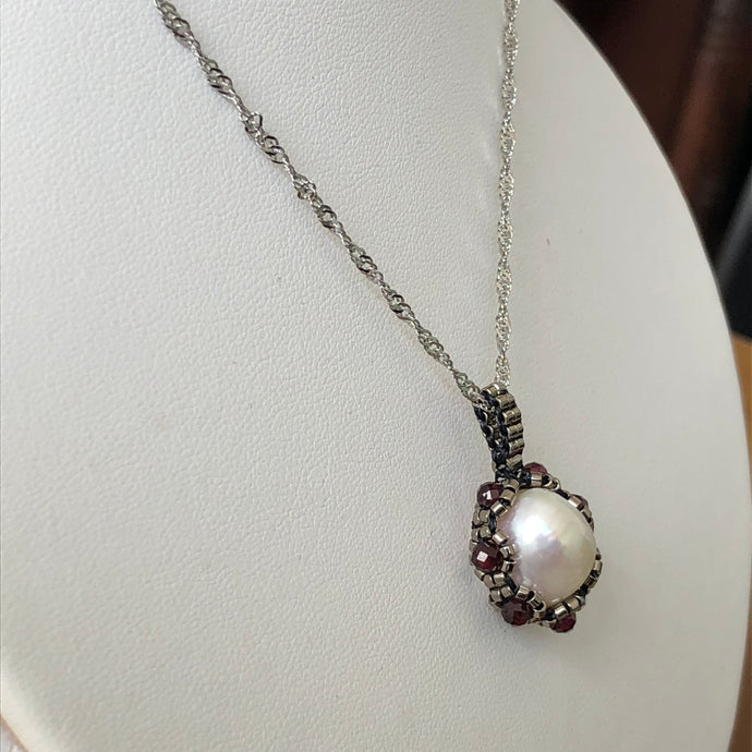 Large baroque freshwater pearl surrounded by metallic micro-beading with facetted garnet, suspended on trace chain.