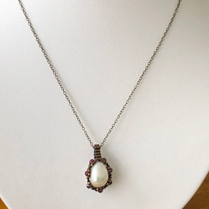 Large baroque freshwater pearl surrounded by metallic micro-beading with facetted garnet, suspended on trace chain.
