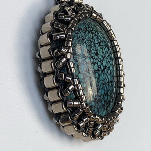 Tibetan Turquoise cabochon pendant framed by a cameo of glass micro-beading in metallic silver tone 