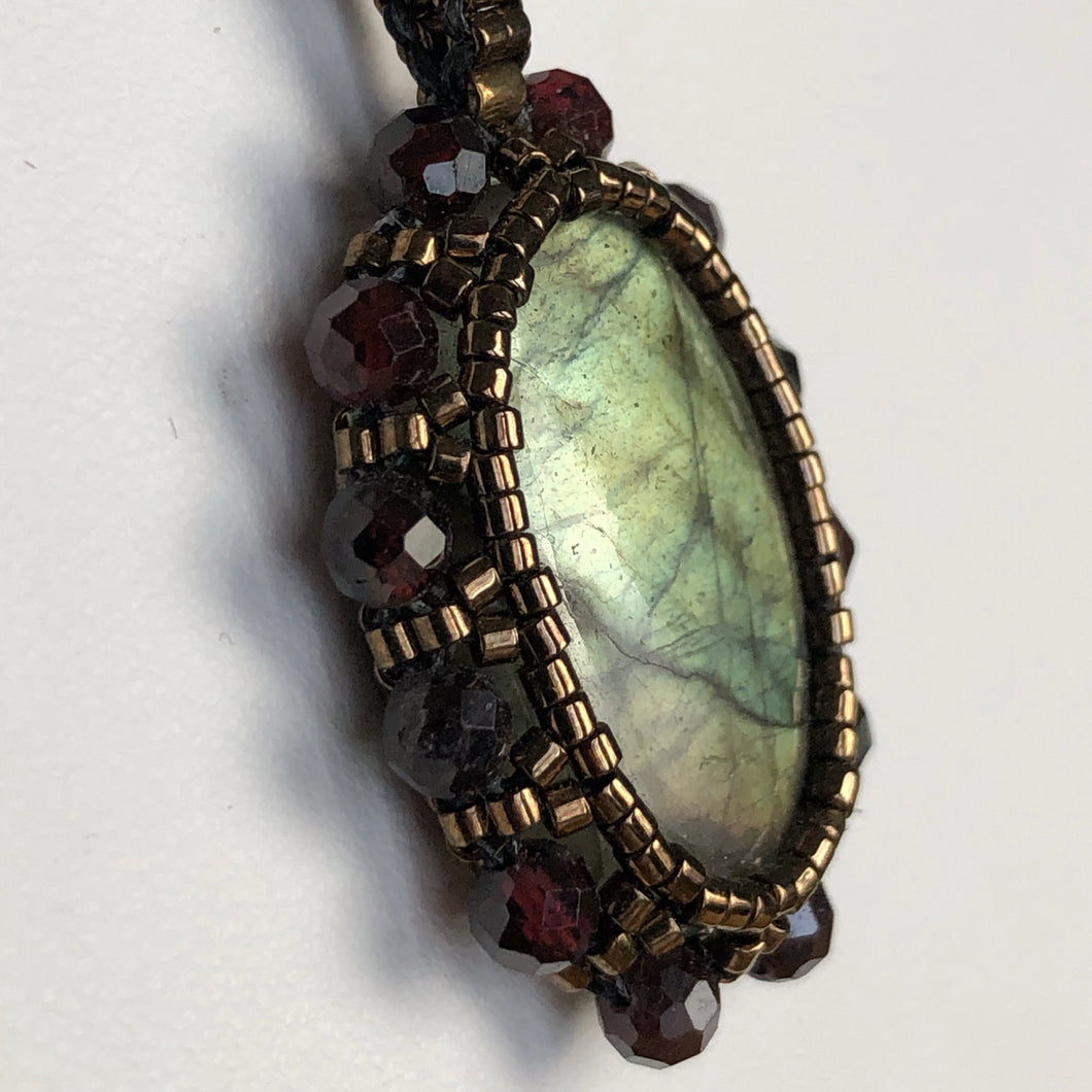 Labradorite cabochon cameo pendant framed by fine beading of metallic bronze micro-beads and garnet gemstone.